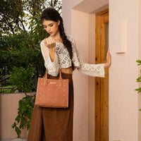WOMEN LOOKING DOWN IN A IVORY CROCKET CROP TOP AND BROWN SKIRT, CARRYING OUR BROWN GRACIE STRUCTURED TOTE  SET IN A MODERN BACKGROUND. 