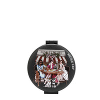 THE FRONT OF THE MIRROR HAS A BLACK BACKGROUND WITH 3 LADIES WEARING DRESSESS AND COATS. SITTING IN FRONT OF A BAKERY DRINKING COFFEE AND EATING BREAD. UNDER THE TABLE THERE'S 2 SCHNAUZER DOGS.