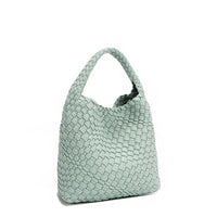 Front angle of Juni handbag crafted in braided vegan leather in pastel, dusty blue with a top handle (5" drop) and open slip compartment secured with a magnetic snap closure. Slouchy, relaxed silhouette offers a chic and laid-back yet refined look.