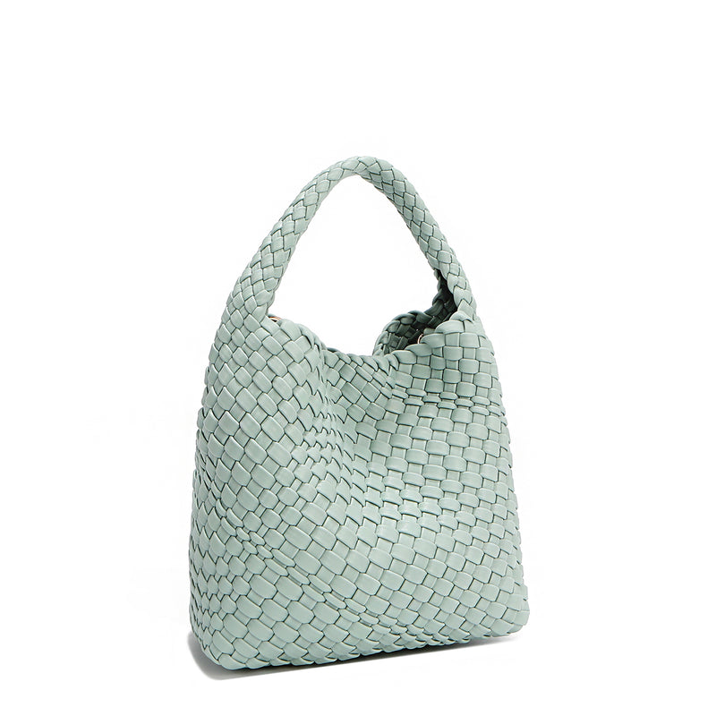 Front angle of Juni handbag crafted in braided vegan leather in pastel, dusty blue with a top handle (5" drop) and open slip compartment secured with a magnetic snap closure. Slouchy, relaxed silhouette offers a chic and laid-back yet refined look.