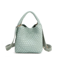 Introducing Juni from Nodu Nadu by Nicole Lee, a versatile and slouchy chic handbag with a removable pouch inside. Crafted in braided vegan leather with an optional, adjustable chevron striped shoulder strap for varied carrying options so you can wear it across the body or by the top handle for a sleek look. Pictured in a pastel, dusty blue shade with a tonal striped shoulder strap.