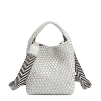 Introducing Juni from Nodu Nadu by Nicole Lee, a versatile and slouchy chic handbag with a removable pouch inside. Crafted in braided vegan leather with an optional, adjustable chevron striped shoulder strap for varied carrying options so you can wear it across the body or by the top handle for a sleek look. Pictured in a silver, metallic shade with a black and white striped shoulder strap.