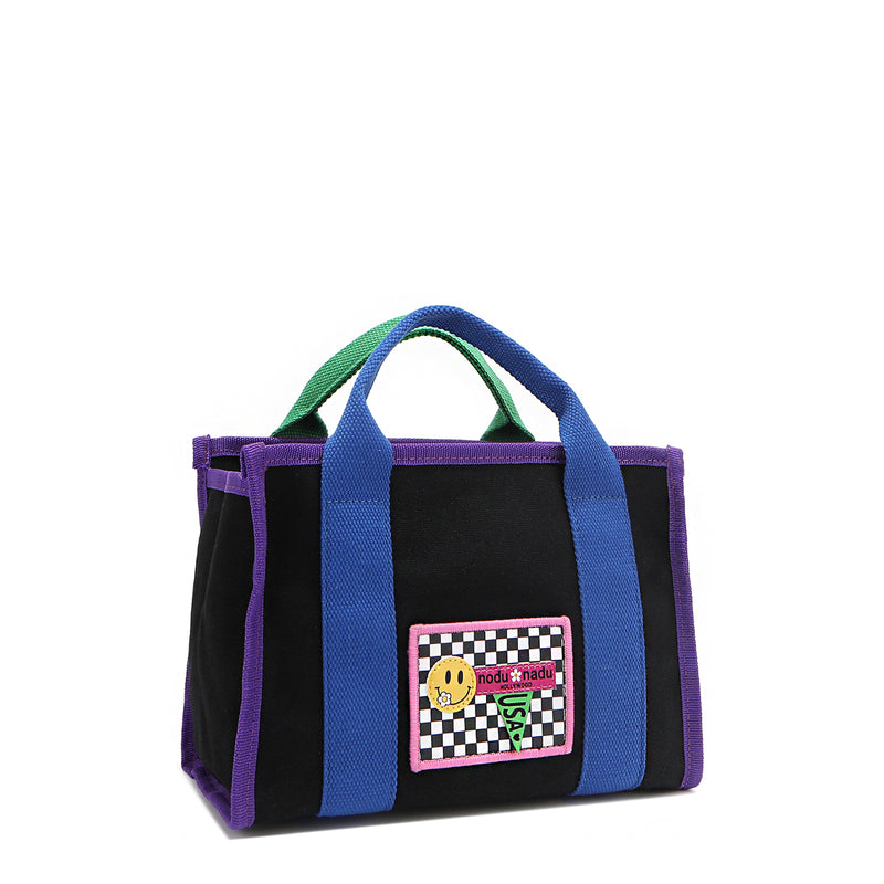 Front angle of the small Rowan polyester bag with bold color-block trim and mix-and-match straps—because your style deserves options! Available in classic black with bold blue and purple accents and a checker print smiley face adorned embroidered logo patch on the front. 