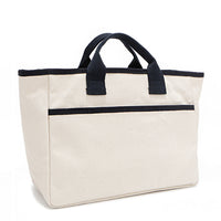 Back angle of the Emery handbag by Nodu Nadu in classic canvas-beige with navy blue trim. Dual top handles and a convenient black slip pocket to keep most-used items like your phone, keys, and planner close at hand. 