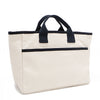 Back angle of the Emery handbag by Nodu Nadu in classic canvas-beige with navy blue trim. Dual top handles and a convenient black slip pocket to keep most-used items like your phone, keys, and planner close at hand. 