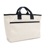 Back angle of the Emery handbag by Nodu Nadu in classic canvas-beige with navy blue trim. Dual top handles and a convenient black slip pocket to keep most-used items like your phone, keys, and planner close at hand. 