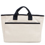 Back angle of the Emery handbag by Nodu Nadu in classic canvas-beige with navy blue trim. Made of polyester with dual top handles and a convenient black slip pocket to keep most-used items like your phone, keys, and planner close at hand. Dual top handles with a 3" drop allow you to carry this handbag by the top handles. 
