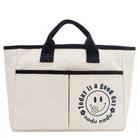 Your daily dose of positivity—now in bag form! With sleek trim details and a feel-good message, this everyday tote is here to remind you that yes, today (and every day) is a good one. Designed for both style and function, it features plenty of compartments inside like 2 front slip pockets. Pictured in classic, canvas-colored beige front angle view for a timeless statement that compliments any look from day to night! Smiley face adorns the front with a cute little flower on its smile. 