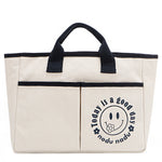 Your daily dose of positivity—now in bag form! With sleek trim details and a feel-good message, this everyday tote is here to remind you that yes, today (and every day) is a good one. Designed for both style and function, it features plenty of compartments inside like 2 front slip pockets. Pictured in classic, canvas-colored beige front angle view for a timeless statement that compliments any look from day to night! Smiley face adorns the front with a cute little flower on its smile. 