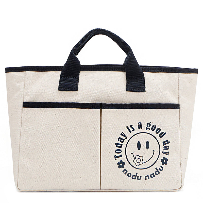 Your daily dose of positivity—now in bag form! With sleek trim details and a feel-good message, this everyday tote is here to remind you that yes, today (and every day) is a good one. Designed for both style and function, it features plenty of compartments inside like 2 front slip pockets. Pictured in classic, canvas-colored beige front angle view for a timeless statement that compliments any look from day to night! Smiley face adorns the front with a cute little flower on its smile. 