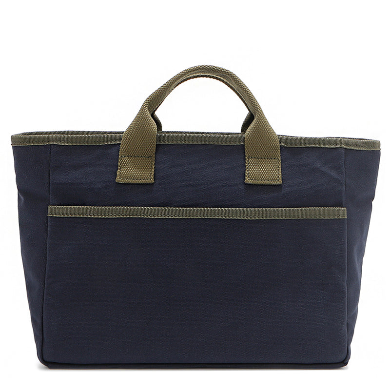 Solid back of the Emery Nodu Nadu tote bag in classic navy blue with moss green trim and dual straps. An open slip compartment in the back allows you to store items like your keys, journal, and more for convenient access. Rectangular silhouette for a classic, timeless feel. 