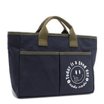 With sleek trim details and a feel-good message, this everyday tote is here to remind you that yes, today (and every day) is a good one. Designed for both style and function, it features plenty of compartments like 2 front slip pockets. Front angle pictured in classic navy blue with moss green trim and straps. White smiley face adorns the front with a cute little flower on its smile in this rectangular silhouette. 