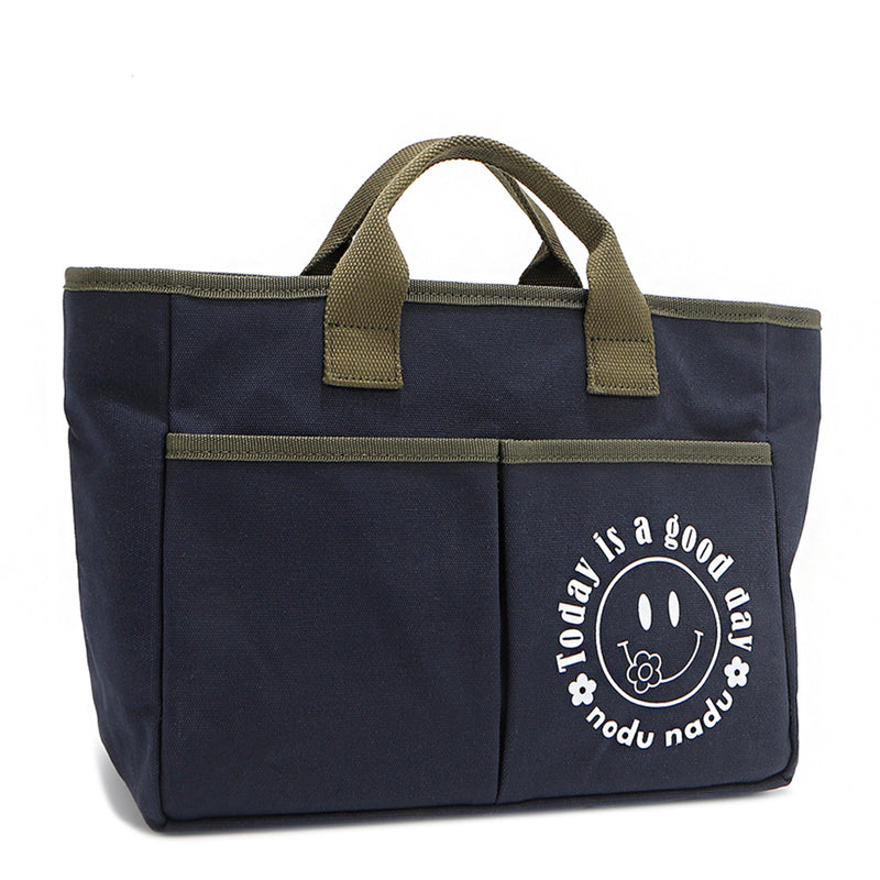 With sleek trim details and a feel-good message, this everyday tote is here to remind you that yes, today (and every day) is a good one. Designed for both style and function, it features plenty of compartments like 2 front slip pockets. Front angle pictured in classic navy blue with moss green trim and straps. White smiley face adorns the front with a cute little flower on its smile in this rectangular silhouette. 