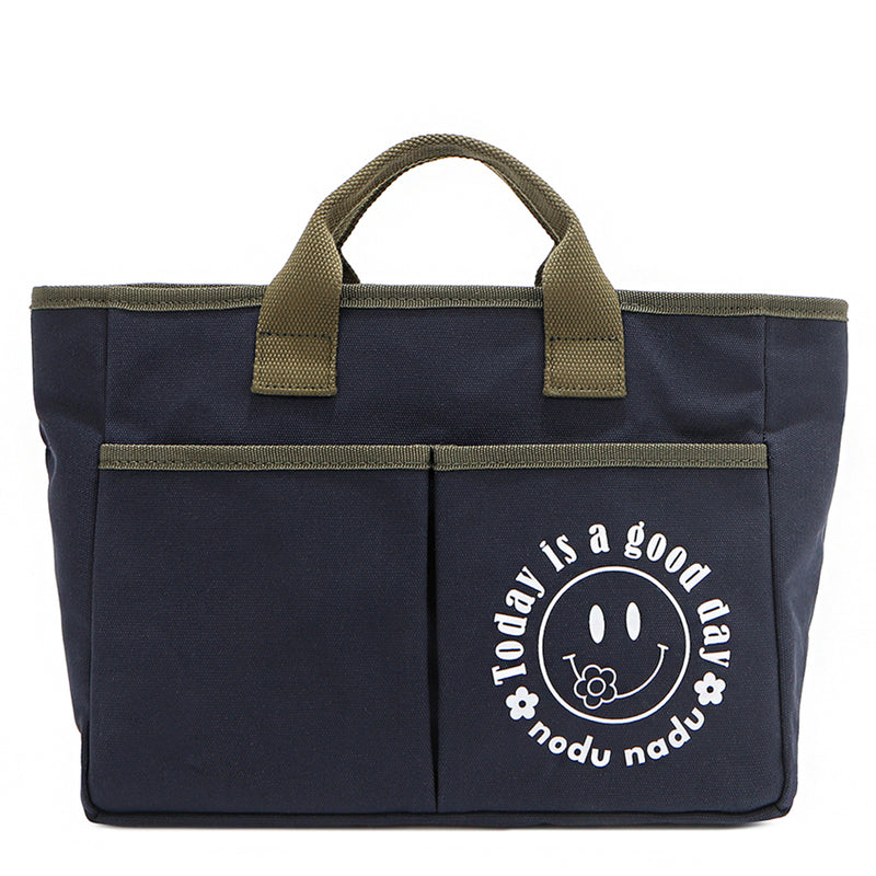 Your daily dose of positivity—now in bag form! With sleek trim details and a feel-good message, this everyday tote is here to remind you that yes, today (and every day) is a good one. Designed for both style and function, it features plenty of compartments like 2 front slip pockets. Pictured in classic navy blue with moss green trim and straps. White smiley face adorns the front with a cute little flower on its smile. 