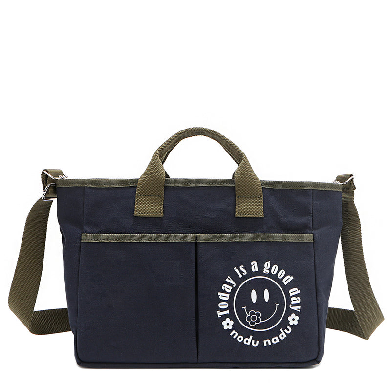 Back angle of the Emery handbag by Nodu Nadu in classic navy blue with moss green trim. Made of polyester with dual top handles and a convenient black slip pocket to keep most-used items like your phone, keys, and planner close at hand. Dual top handles with a 3" drop and an optional, adjustable shoulder strap allow you to carry this tote by the top handles as a handbag or across the body as a crossbody or shoulder bag! The options are endless to mix and match according to your style needs. 