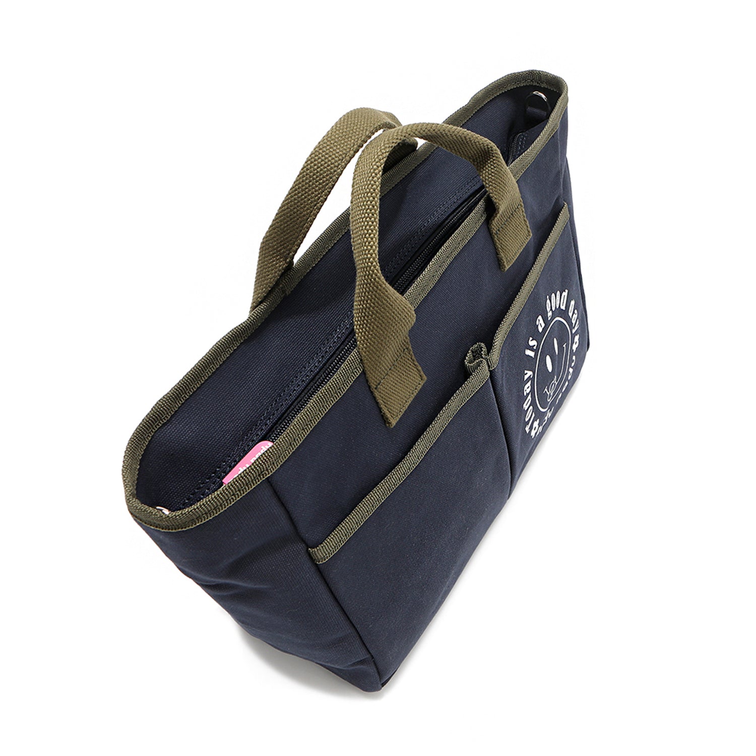 Top angle of the Emery Nodu Nadu tote bag in navy blue with moss green trim and dual handles. Two front slip pockets with a "today is a good day" with a happy smiley face on one of the front pockets. A recessed zip top closure with a pink zipper keeps possessions secure. 