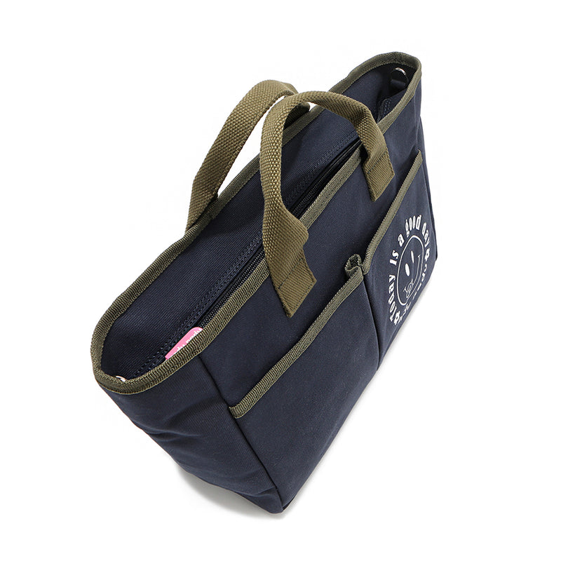 Top angle of the Emery Nodu Nadu tote bag in navy blue with moss green trim and dual handles. Two front slip pockets with a "today is a good day" with a happy smiley face on one of the front pockets. A recessed zip top closure with a pink zipper keeps possessions secure. 
