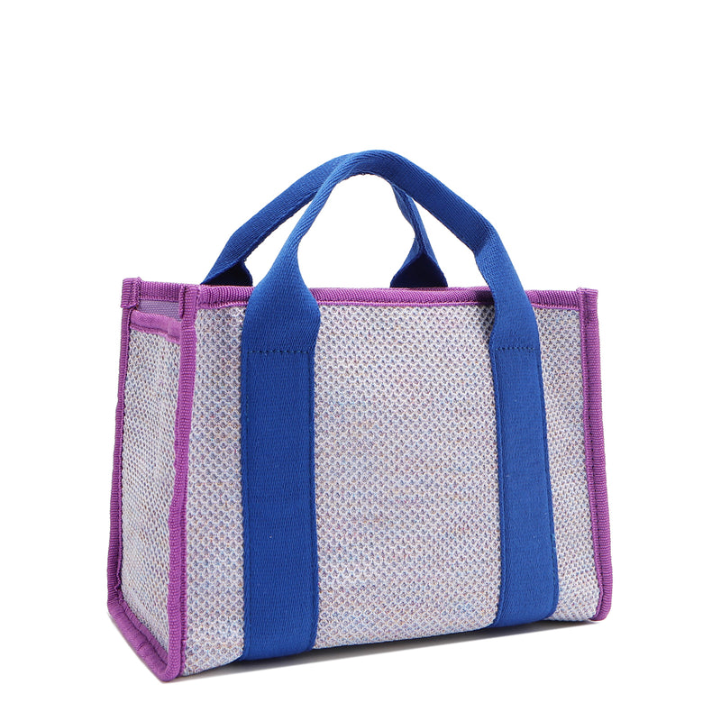 Back angle view of the Nodu Nadu small canvas Marley tote Bag in lavender. Accented with bold electric blue straps and a gorgeous purple trim, this canvas features a subtle metallic shimmer that hits the light whenever you walk for a head-turning detail. 