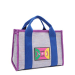 Front angle view of the Nodu Nadu small Marley tote bag in lavender.  Featuring dual top handles with a 3.5" drop and adorned with a logo stitched nodu nadu patch with a smiley face and sad face. Metallic shimmering light lavender canvas with bold electric blue strap accents complimented with a vibrant purple trim. 