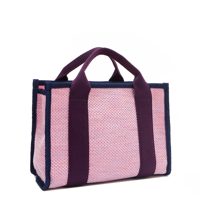 Back angle view of the Nodu Nadu small canvas Marley tote Bag in pink. Accented with eggplant purple straps and a navy blue trim, this canvas features a subtle metallic shimmer that hits the light whenever you walk for a head-turning detail. 