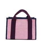 Back view of the Nodu Nadu small canvas Marley tote Bag in pink. Accented with eggplant purple straps and a navy blue trim, this canvas features a subtle metallic shimmer that hits the light whenever you walk for a head-turning detail. 