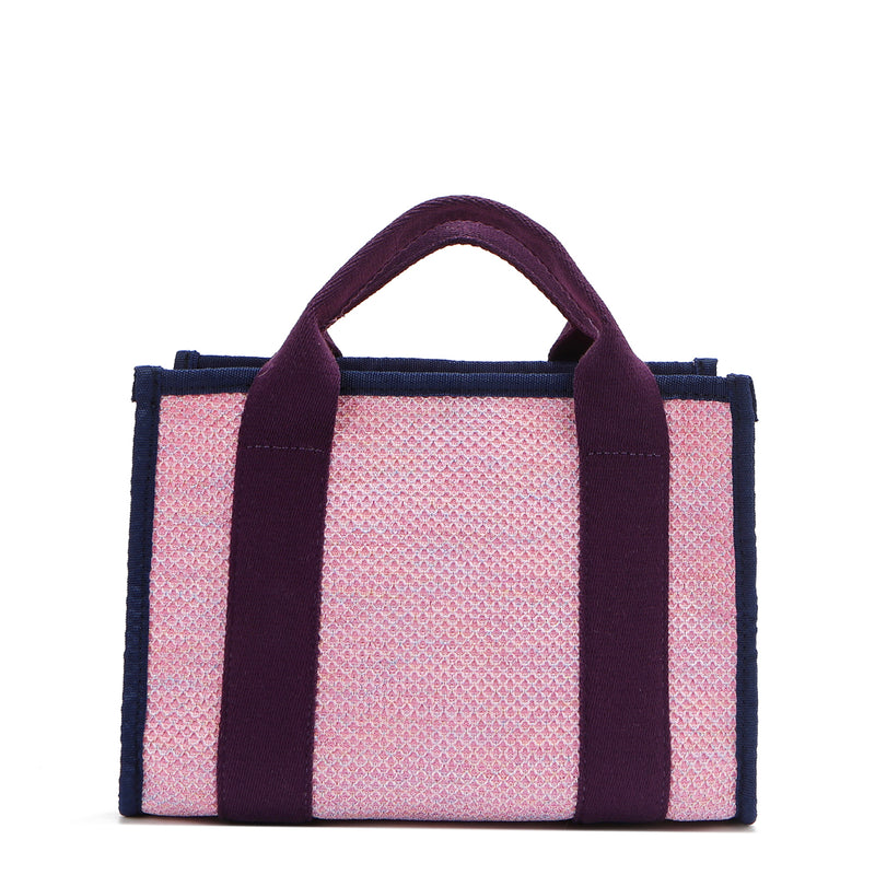 Back view of the Nodu Nadu small canvas Marley tote Bag in pink. Accented with eggplant purple straps and a navy blue trim, this canvas features a subtle metallic shimmer that hits the light whenever you walk for a head-turning detail. 
