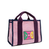 Front angle view of the Nodu Nadu small Marley tote bag in pink.  Featuring dual top handles with a 3.5" drop and adorned with a logo stitched nodu nadu patch with a smiley face and sad face. Metallic shimmering light pink canvas with eggplant purple strap accents complimented with a navy blue trim. 