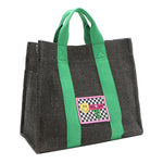 Front angle view of the Nodu Nadu Sawyer Bag in Black with grass green strap accents. Charcoal black canvas adorned with a stitched logo patch in black and white checker print with nodu nadu smiley face. Front angle shows the side slip pocket to store essentials that you want close within reach like your phone, keys, wallet, lipstick, and more!