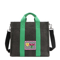 Nodu Nadu Sawyer Bag in Black with grass green strap accents and paired with an adjustable, optional black wide shoulder strap. Wear this bag by the top handles or across the body thanks to the versatile shoulder strap options. 