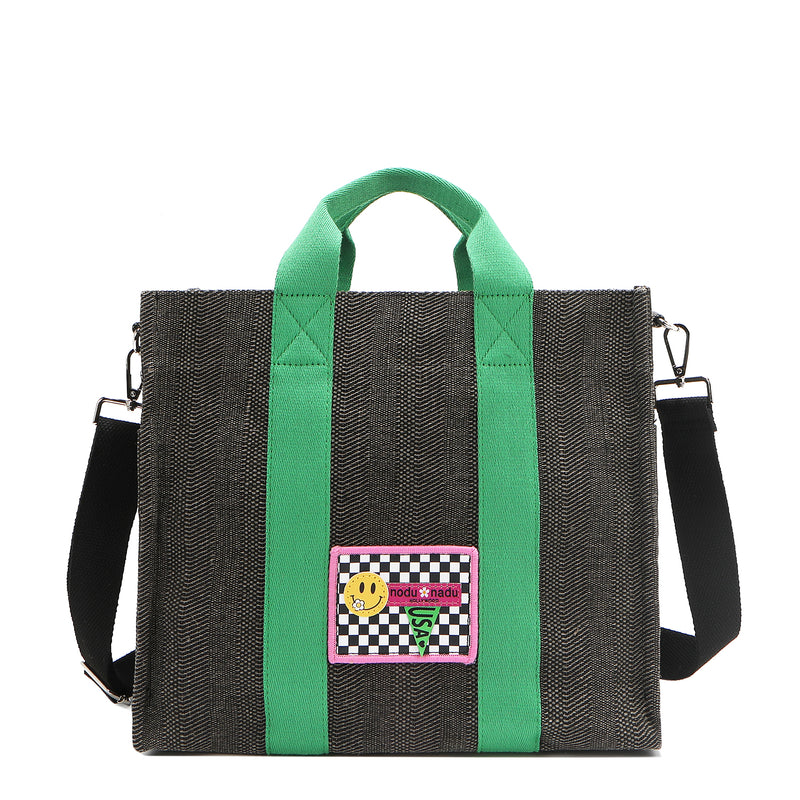 Nodu Nadu Sawyer Bag in Black with grass green strap accents and paired with an adjustable, optional black wide shoulder strap. Wear this bag by the top handles or across the body thanks to the versatile shoulder strap options. 