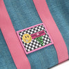 Close-up macro detail shot of the Nodu Nadu Sawyer Bag in Blue. Baby pink strap accents adorn this canvas everyday bag. The front is adorned with an embroidered stitch logo patch in a black and white checker print with a nodu nadu smiley face and daisy flower on its smile. Nodu Nadu tag made in hollywood with a green USA flag to showcase our proud origins. 