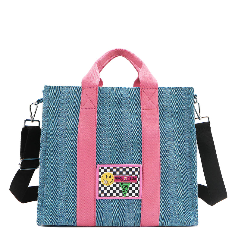 Nodu Nadu Sawyer Bag in Blue with baby pink accents and a black and white checker print embroidered stitch logo with a smiley face. Paired with a black adjustable and detachable wide shoulder strap for varied carrying options and versatility to switch up your style needs with ease. 