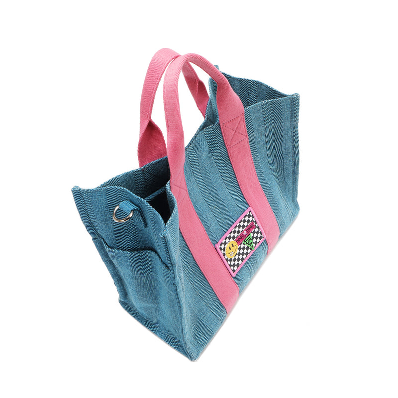 Top angle of the Nodu Nadu Sawyer Bag in blue with baby pink dual handles and a checker print stitched logo with a smiley face. Side D-ring for optional shoulder strap attachment and side slip pocket to store everyday must-haves like makeup, wallet, keys, and more conveniently within reach! 