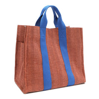 Back angle view of the Nodu Nadu Sawyer Bag in Orange/Sienna brown with bold blue accents. Rectangular side view of the canvas bag shows the side slip pocket that can store any essentials you want close at hand. 