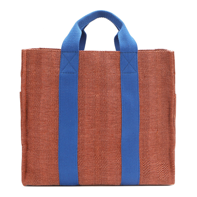 Back of the Nodu Nadu Sawyer Bag in Orange. Orange/sienna brown-colored canvas accented with bold electric blue straps for a pop of trendy color and vibrance. Rectangular silhouette provides a sense of classic timelessness so you can dress up or dress down this everyday style. 