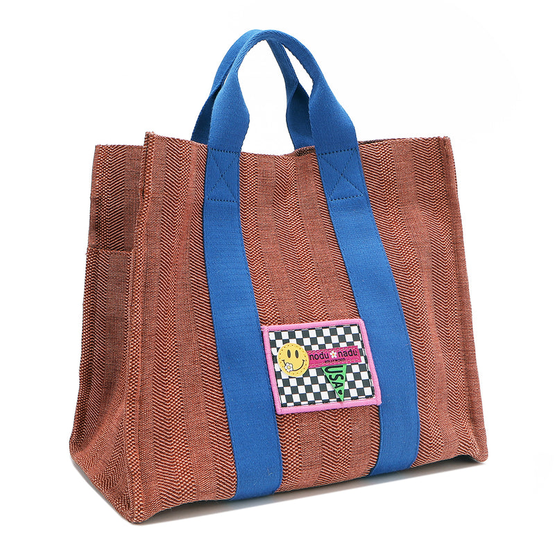 Front angle view of the Nodu Nadu Sawyer Bag in Orange. Crafted in durable canvas with side D-rings for optional shoulder strap attachment so you can wear this bag as a handbag, shoulder bag, or crossbody! It also features side slip pockets for a convenient touch. 