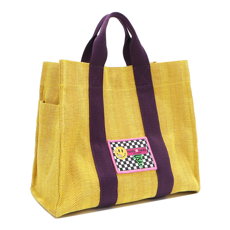 Front angle view of the Nodu Nadu Sawyer Bag in Yellow. Crafted in durable canvas with side D-rings for optional shoulder strap attachment so you can wear this bag as a handbag, shoulder bag, or crossbody! It also features side slip pockets for a convenient touch. 