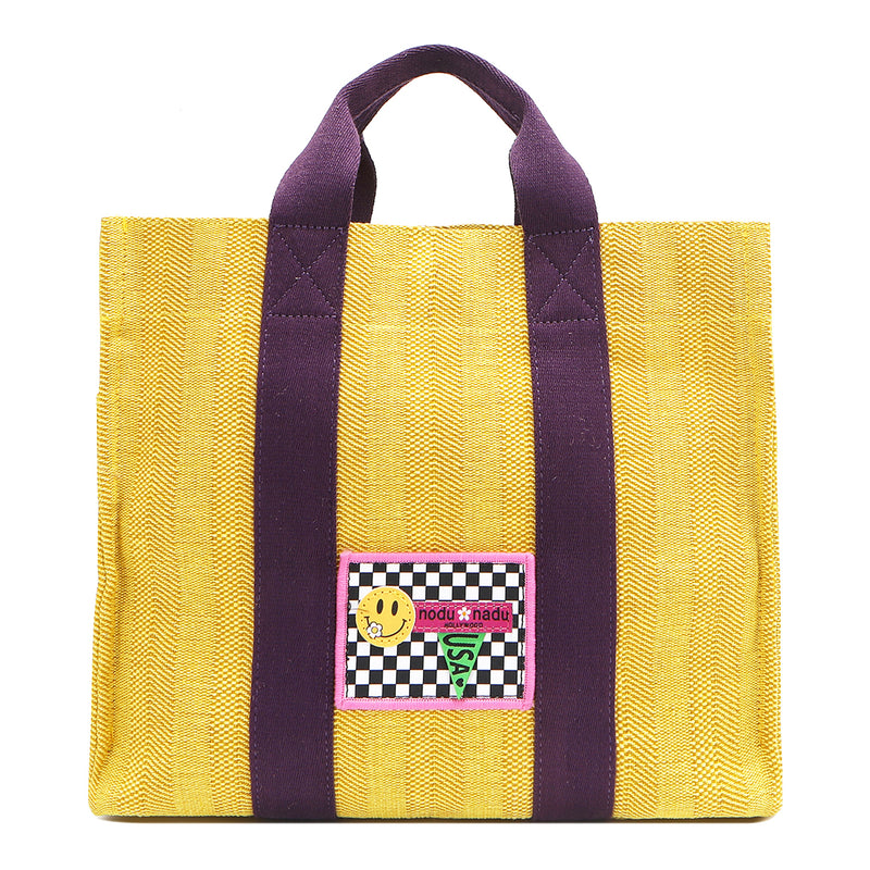 Your must-have carryall for school, weekends, and everything in between! Designed with a soft, relaxed silhouette, the Nodu Nadu Sawyer in Yellow offers plenty of space to keep notebooks and loose essentials effortlessly organized—so you're always ready to grab and go! Sunny yellow canvas paired with eggplant purple strap accents. 