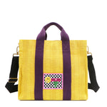 Nodu Nadu Sawyer Bag in Yellow with eggplant purple strap accents and paired with an adjustable, optional black wide shoulder strap. Wear this bag by the top handles or across the body thanks to the versatile shoulder strap options. 