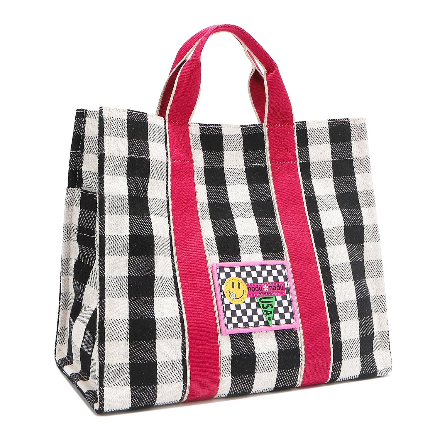 Angled front view of the Nodu Nadu Canvas Blair Bag in Black – highlighting pink handles, side panel with open slip pocket, and checkered embroidered patch with smiley face and nodu nadu stitch logo.