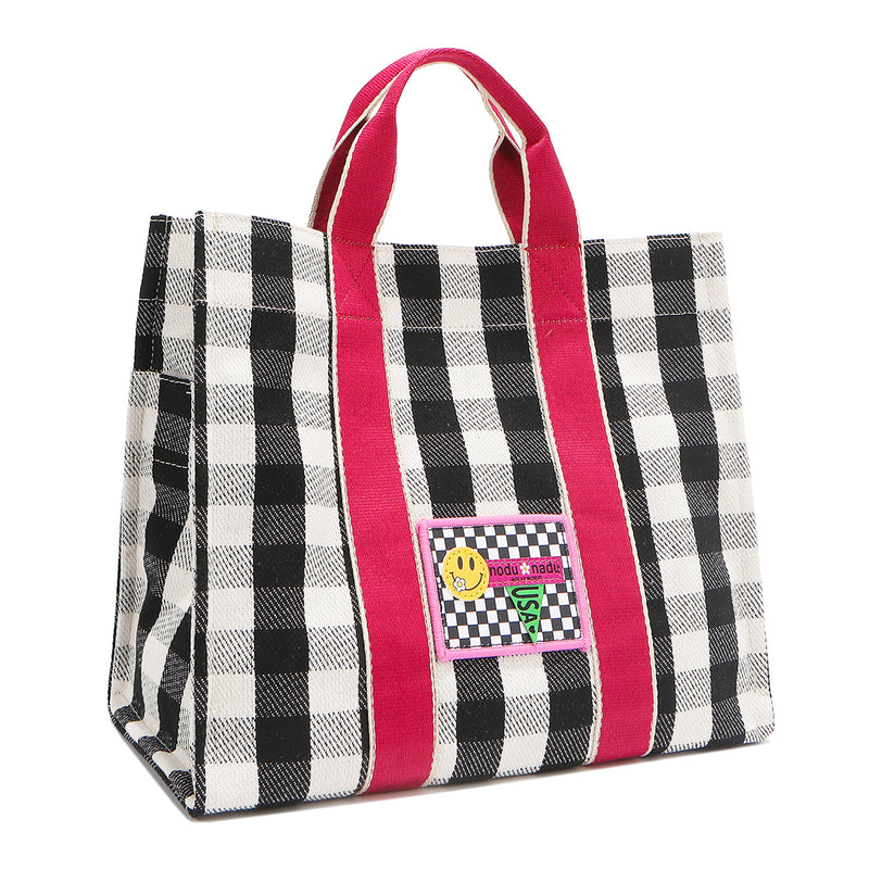 Angled front view of the Nodu Nadu Canvas Blair Bag in Black – highlighting pink handles, side panel with open slip pocket, and checkered embroidered patch with smiley face and nodu nadu stitch logo.
