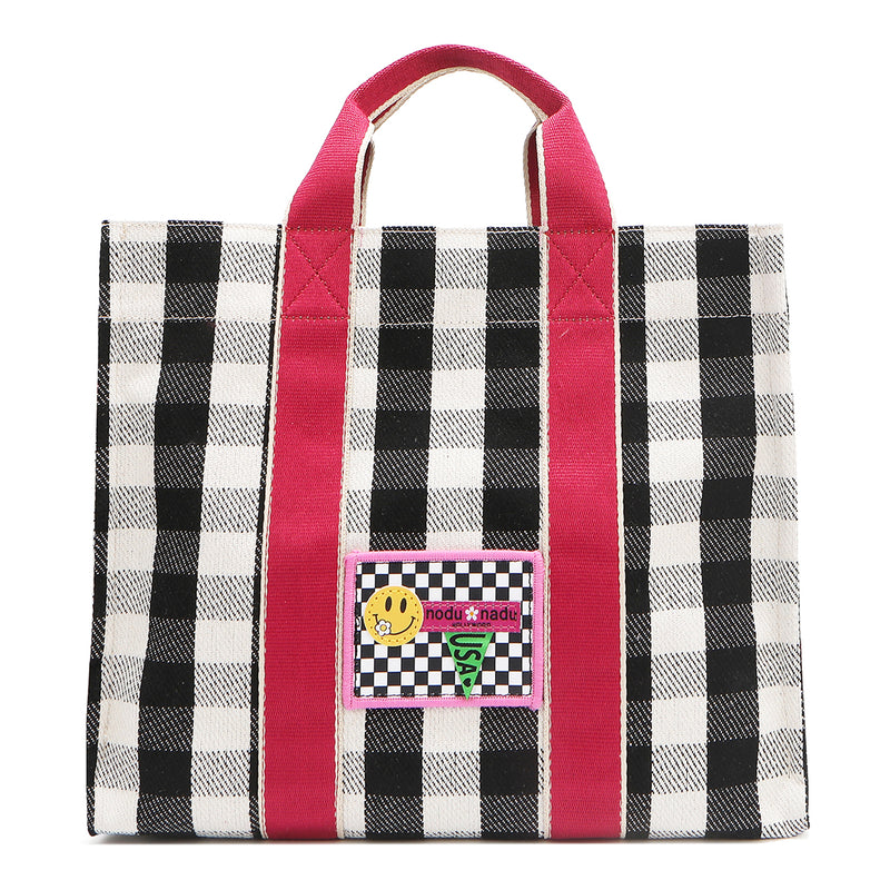 Nodu Nadu Canvas Blair Bag in Black – Stylish black and white checkered tote with bold pink handles, featuring a playful front patch design and durable canvas construction, perfect for everyday use or casual outings.