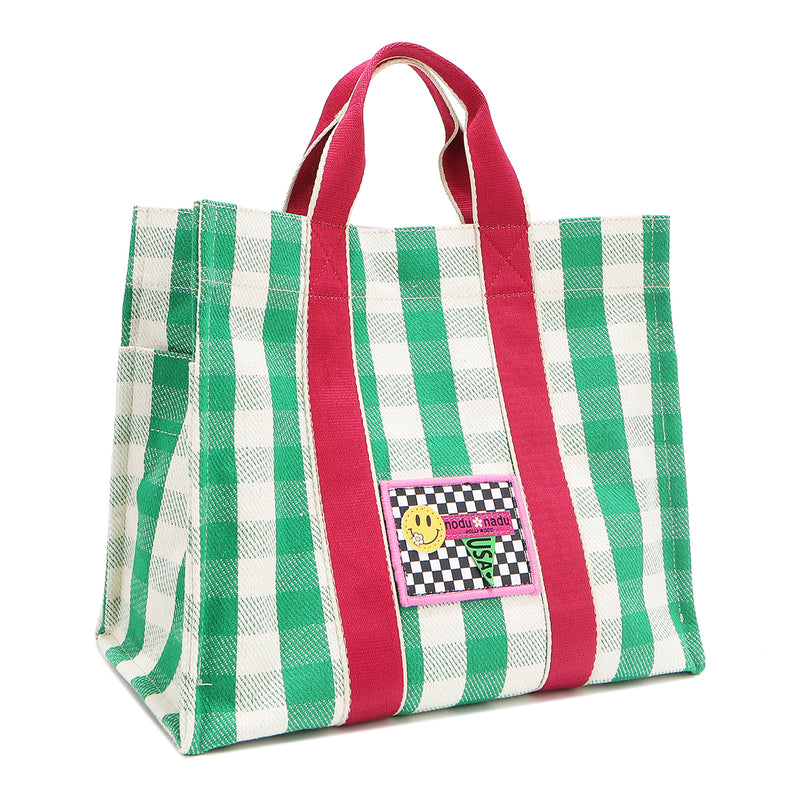 Angled front view of the Nodu Nadu Canvas Blair Bag in Green – highlighting pink handles, side panel with open slip pocket, and checkered patch. 