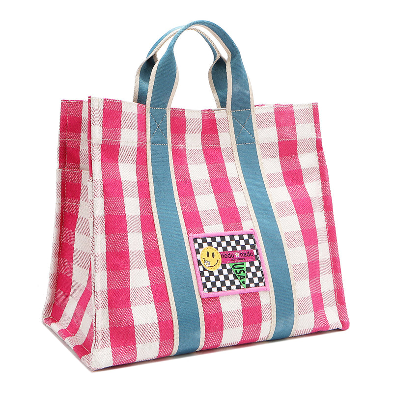 Front angle of the Nodu Nadu Blair Canvas Bag in pink. Made of durable canvas and designed in Los Angeles, California. Bold pink and white gingham print paired with sky blue straps make for a sweet and feminine look! Rectangular silhouette for a timeless finish.
