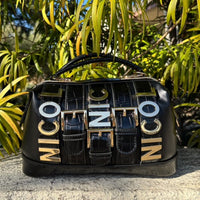 A lifestyle product shot of a black Nicole Lee Calista handbag with plants and foliage in the background. 