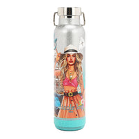 THE TUMBLER HAS A CYLINDRICAL SHAPE WITH A SCREW CAP, IN MARTHA TRAVELS ITALY PRINT. IT HAS A SILVER GLITTER BACKGROUND. THE FRONT HAS THE IMAGE OF A BLONDE GIRL TOUCHING HER HAT AND HOLDING A CUP WITH A HANDBAG ON HER ARM. AT THE BOTTOM IS A BLUETOOTH SPEAKER COLOR MINT