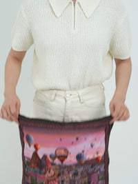 A WOMEN SHOWING OW TO UNFOLD AND FOLD BACK OUR TRAVEL PILLOW BLANKET IN OUR HEAVEN ON EARTH DESIGN. FOR REFERENCE OUR HEAVEN ON EARTH DESIGN IS OUT OF STOCK.